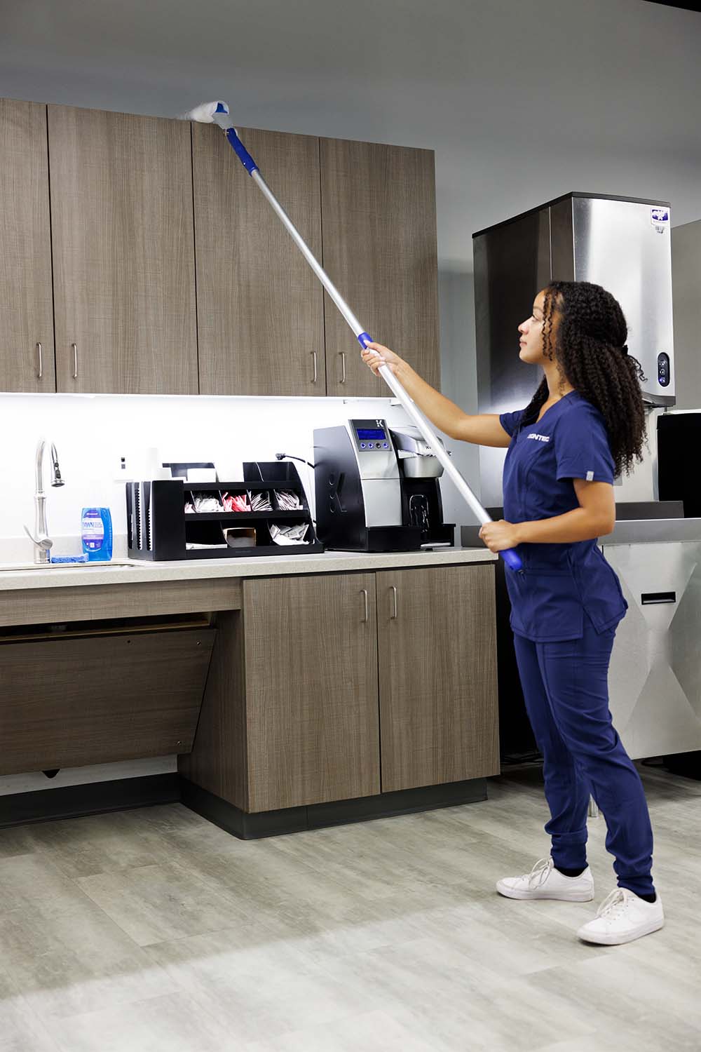 nurse in navy scrubs mopping top of wood cabinets