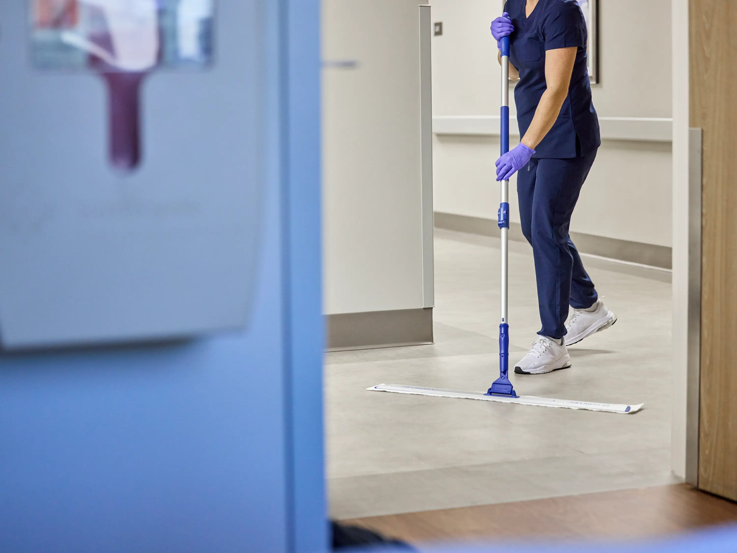 Environmental services worker mopping the floor in a healthcare facility corridor.