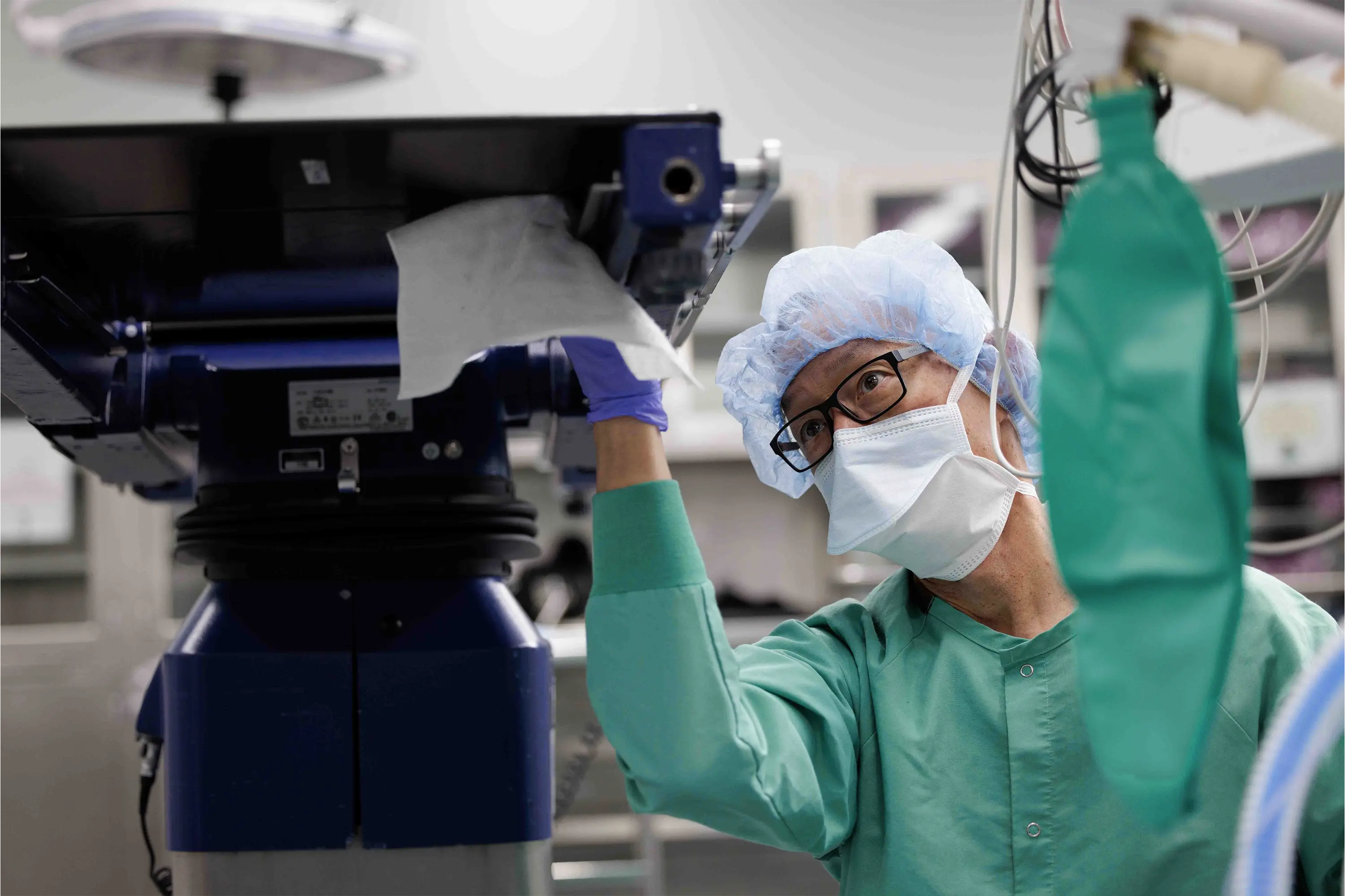 Healthcare worker in surgical attire wiping the underside of an operating room table.