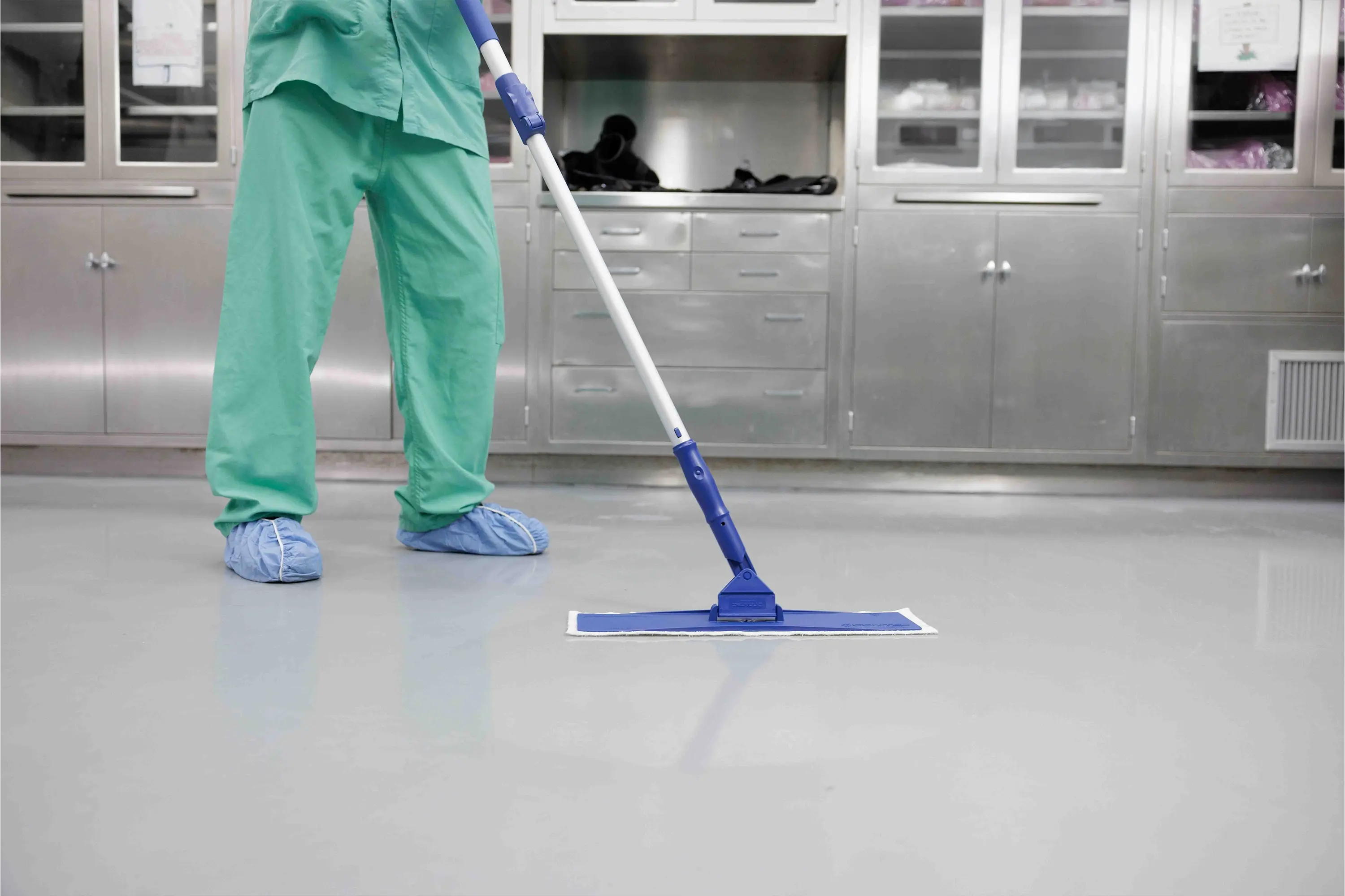 Healthcare worker in surgical attire mopping the floor inside an operating room.