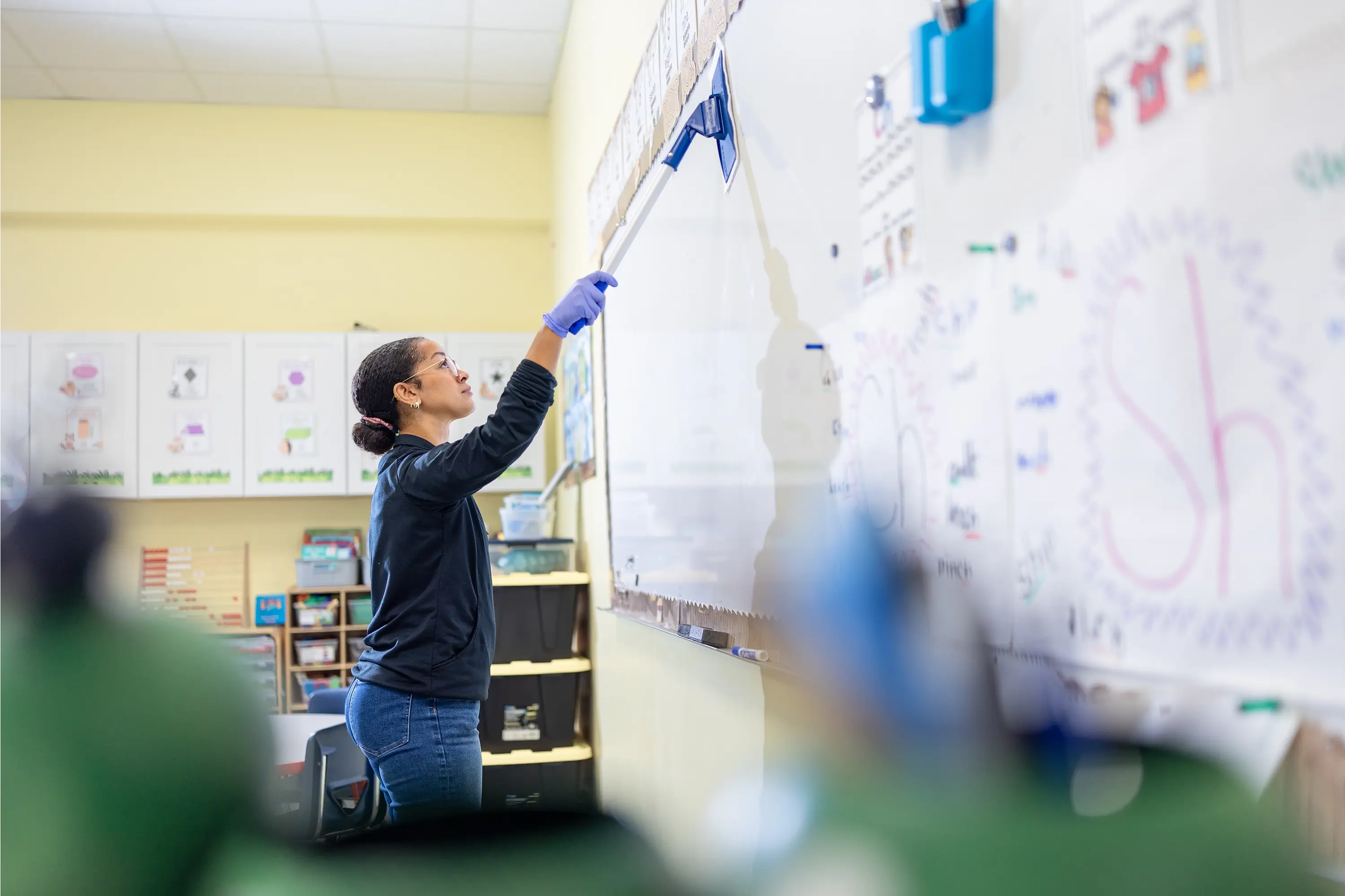Worker using an extendable cleaning tool to clean a whiteboard in a classroom.